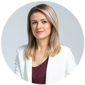 Portrait of a woman with shoulder-length blond hair, wearing a white blazer over a burgundy top, looking at the camera in a neutral pose.